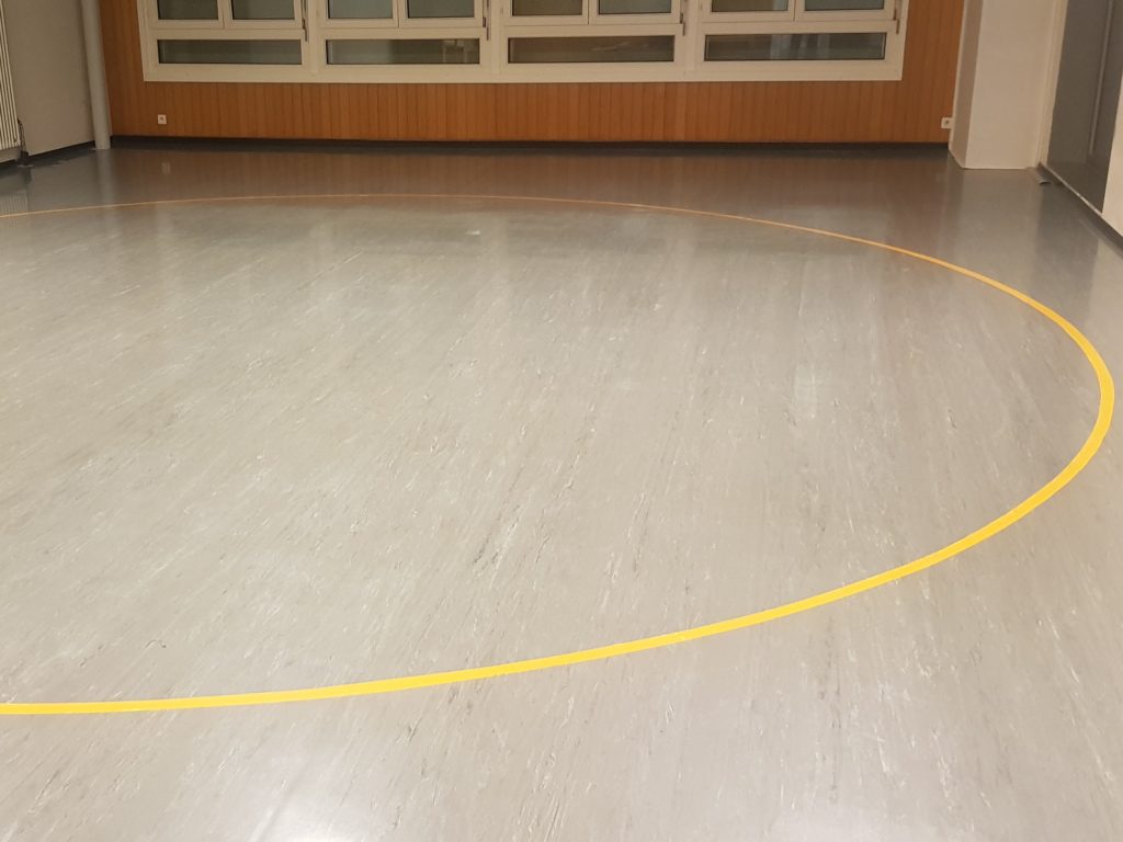 Ancien revêtement PVC gris et rayé dans une salle de rythmique, avant son remplacement