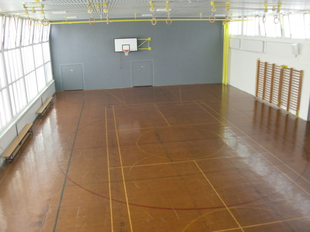 Ancien revêtement de sol usé et rayé dans une salle de gymnastique scolaire