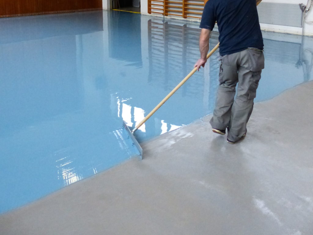 Application de la résine polyuréthane bleue à la raclette sur un sol sportif