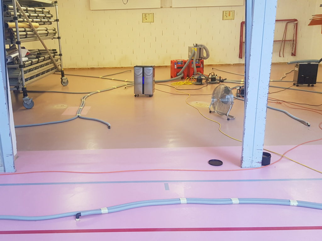 Assèchement en cours dans les locaux de rangement d'une salle de sport, déshumidificateurs et gaines posés sur le sol