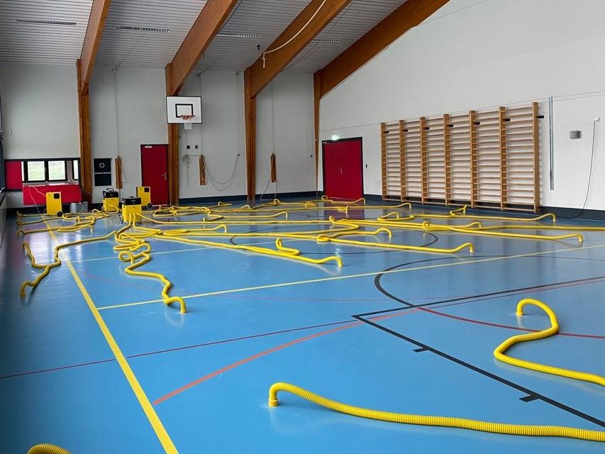 Salle de sport pendant l'assèchement du sol, gaines jaunes réparties sur la surface de jeu et reliées aux déshumidificateurs