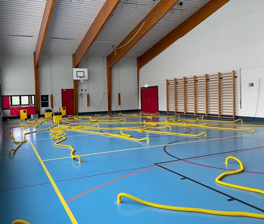 Salle de sport pendant l'assèchement du sol, gaines jaunes réparties sur la surface de jeu et reliées aux déshumidificateurs