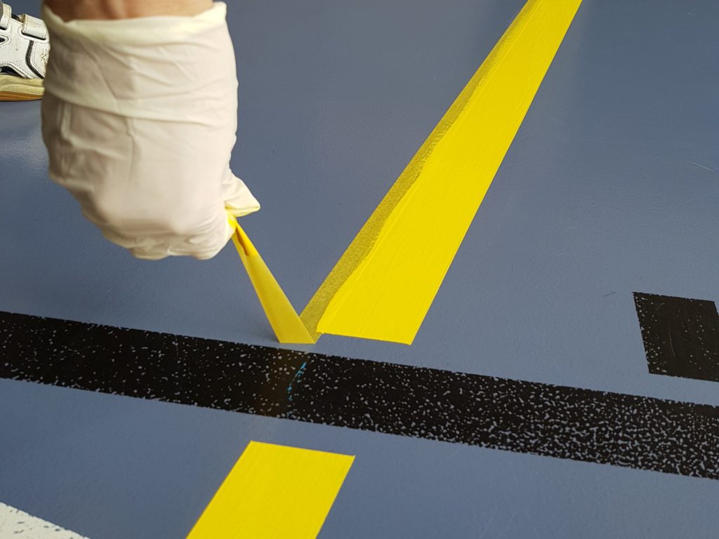 Ruban de masquage retiré à l'angle d'une ligne jaune, bord de peinture net sur un sol sportif