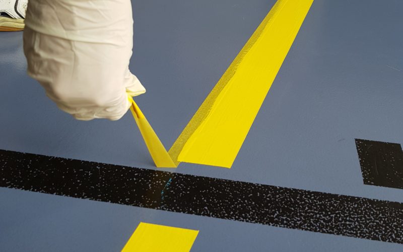 Ruban de masquage retiré à l'angle d'une ligne jaune, bord de peinture net sur un sol sportif