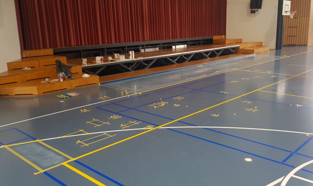 Salle polyvalente pendant la rénovation de son sol, zones délimitées au ruban devant la scène et matériel posé sur les marches