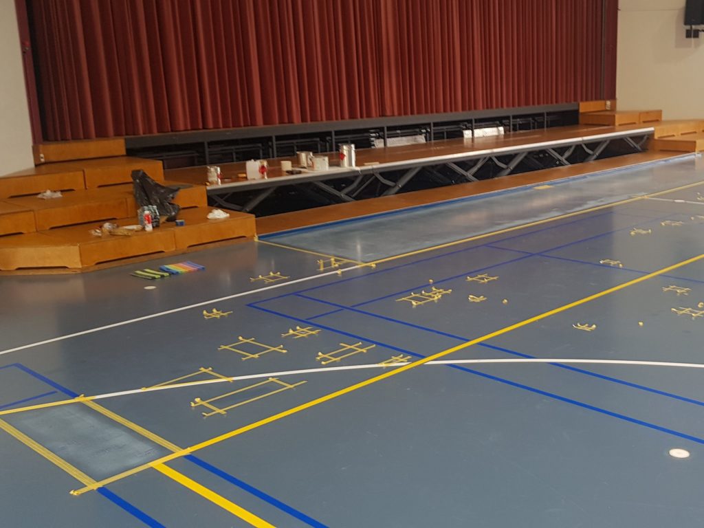 Salle polyvalente pendant la rénovation de son sol, zones délimitées au ruban devant la scène et matériel posé sur les marches