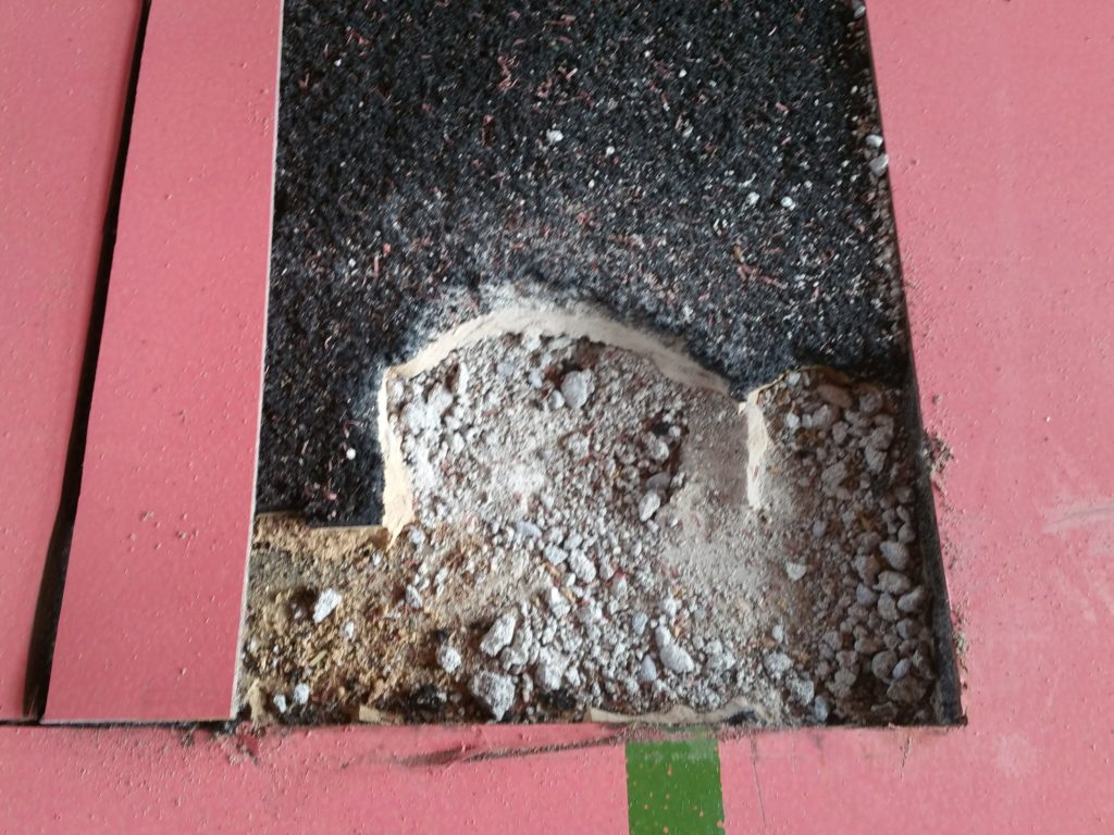 Zone découpée d'un sol sportif, chape en ciment effritée en gravats sous la sous-couche en caoutchouc après des chocs d'haltères
