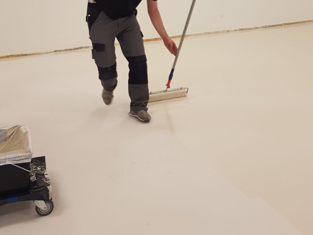 Application au rouleau de la couche de finition claire sur un sol sportif en résine
