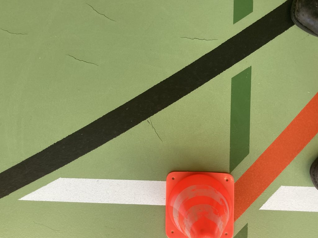 Déchirures dans un revêtement sportif en résine polyuréthane vert, entre les lignes de jeu d'une salle de gymnastique