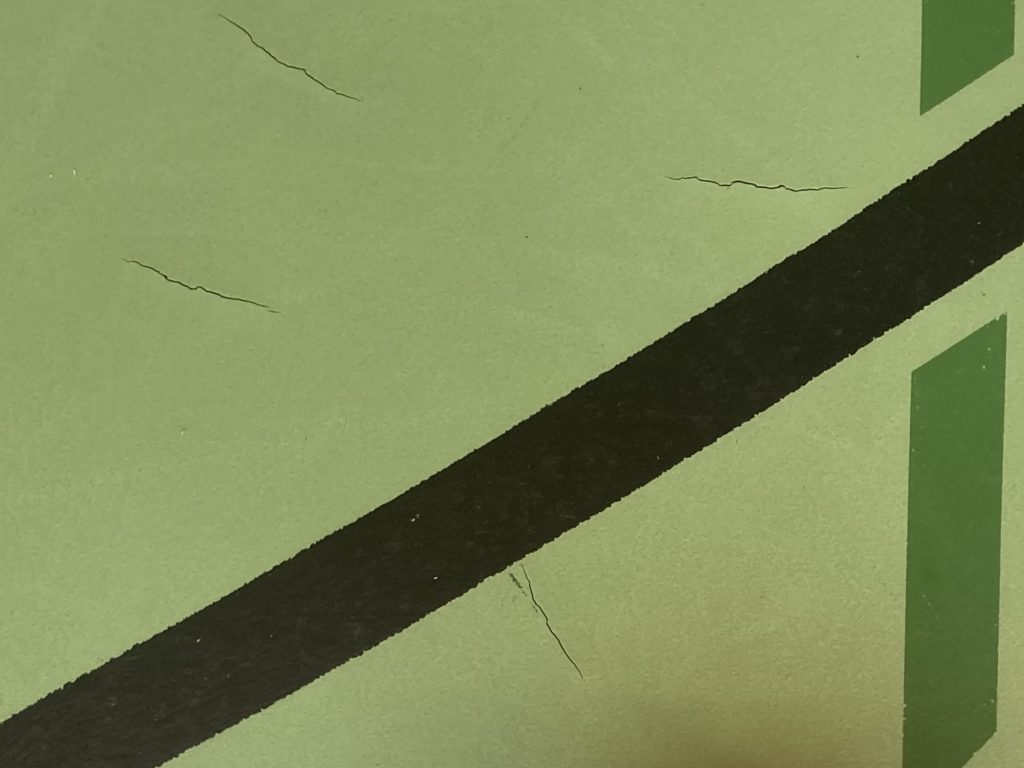 Déchirures dans un revêtement sportif en résine polyuréthane vert, entre les lignes de jeu d'une salle de gymnastique