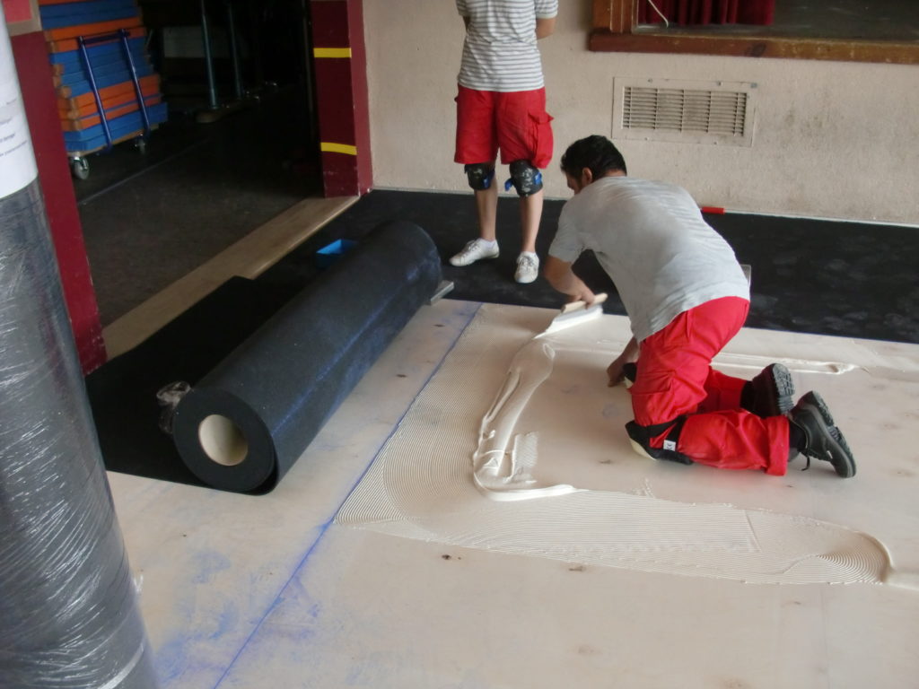 Encollage du plancher sportif et déroulage de la sous-couche souple noire