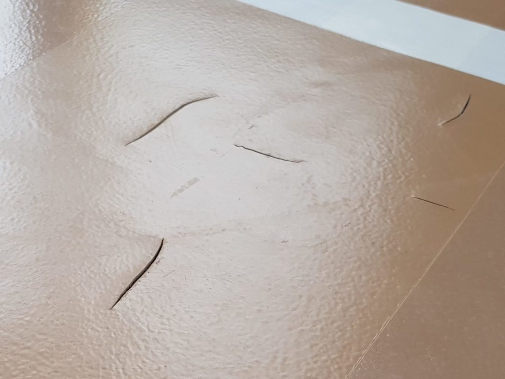 Fissures ouvertes dans le revêtement d'un sol sportif sans joint, près d'une ligne de jeu verte