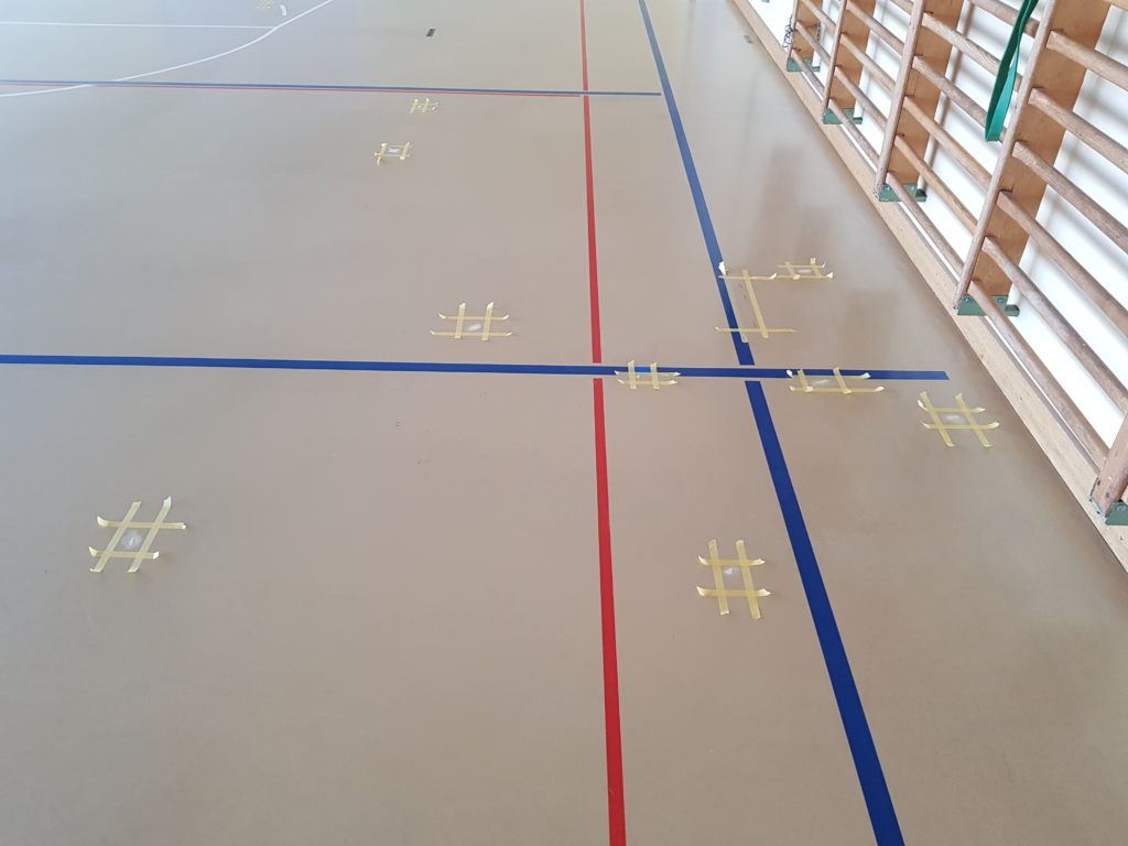 Fissures d'un sol sportif reprises une à une en résine polyuréthane, chaque zone délimitée par du ruban de masquage