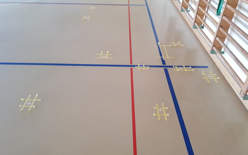 Fissures d'un sol sportif reprises une à une en résine polyuréthane, chaque zone délimitée par du ruban de masquage
