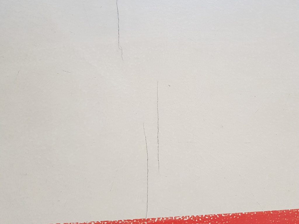 Fissures ouvertes dans le revêtement en résine d'un sol sportif, près d'une ligne de jeu rouge
