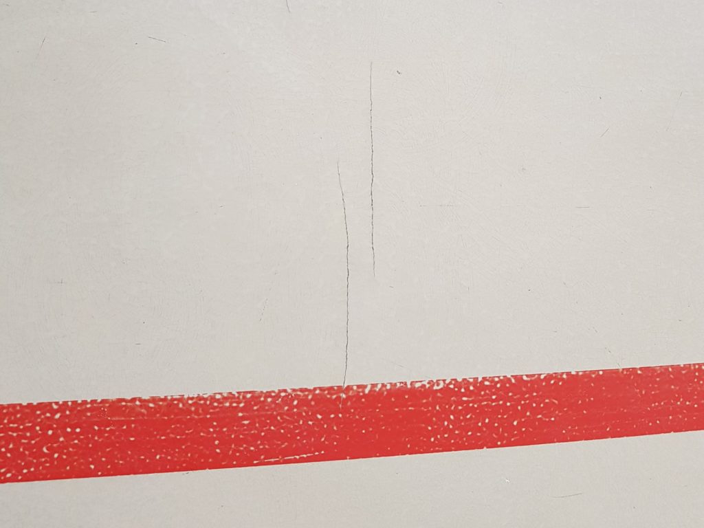 Fissures ouvertes dans le revêtement en résine d'un sol sportif, près d'une ligne de jeu rouge