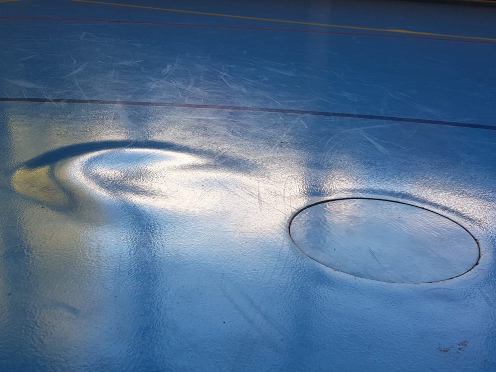 Très grosse cloque dans le revêtement d'un sol sportif, à côté d'un couvercle de douille, après un dégât d'eau passé inaperçu