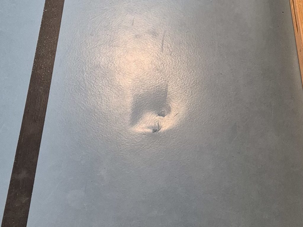 Enfoncement dans le revêtement d'un sol sportif provoqué par la chute d'un vitrage, près du bord de la salle