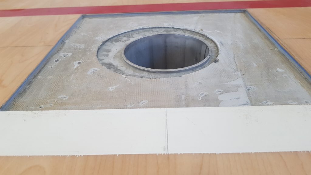 Nouvelle douille d'engin implantée dans un sol sportif en PVC décor bois, support mis à nu autour de la douille