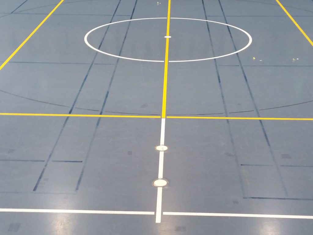 Salle de sport avant remarquage, lignes de badminton bleu foncé à peine visibles sur le sol bleu