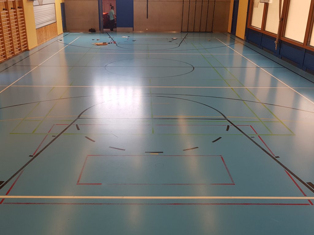 Salle polyvalente avant remarquage, lignes de jeu presque effacées sur un plancher souple