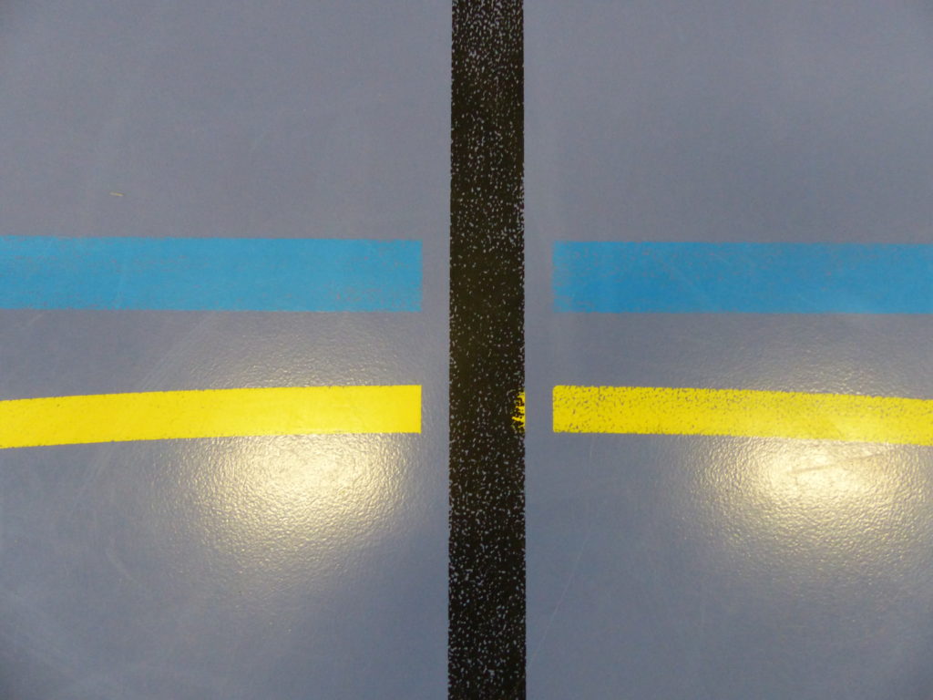 Anciennes lignes de volley bleues peu contrastées sur un sol sportif bleu violet, ligne jaune voisine usée