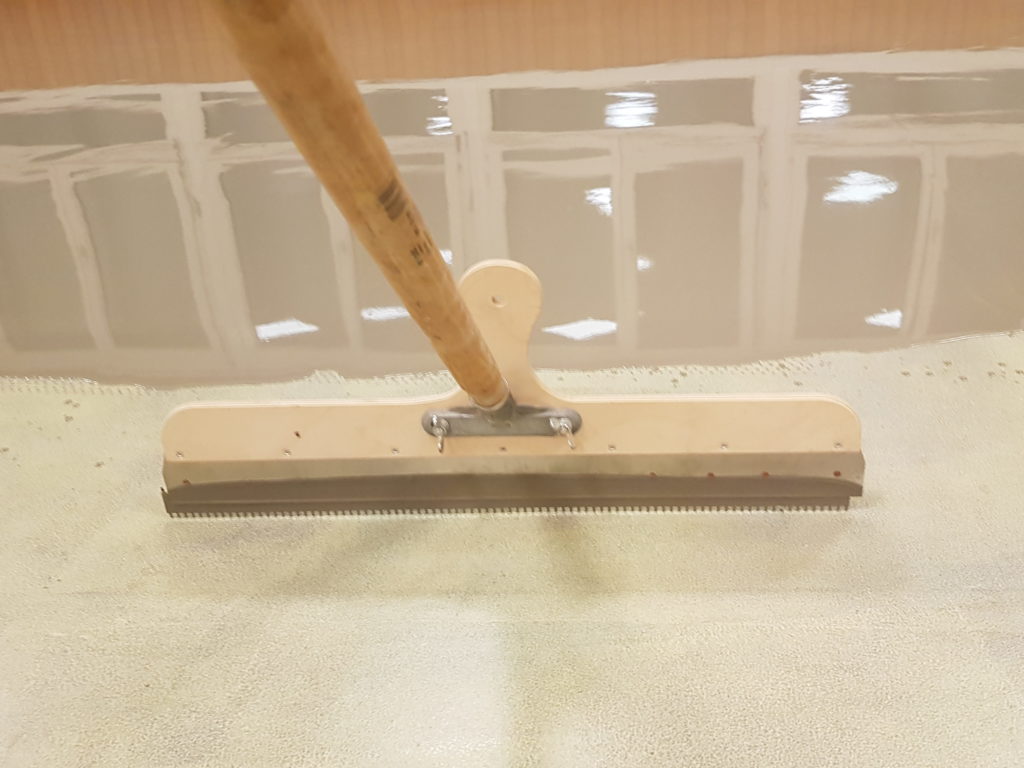 Lissage du support à la raclette crantée avant la pose d'un sol sportif souple