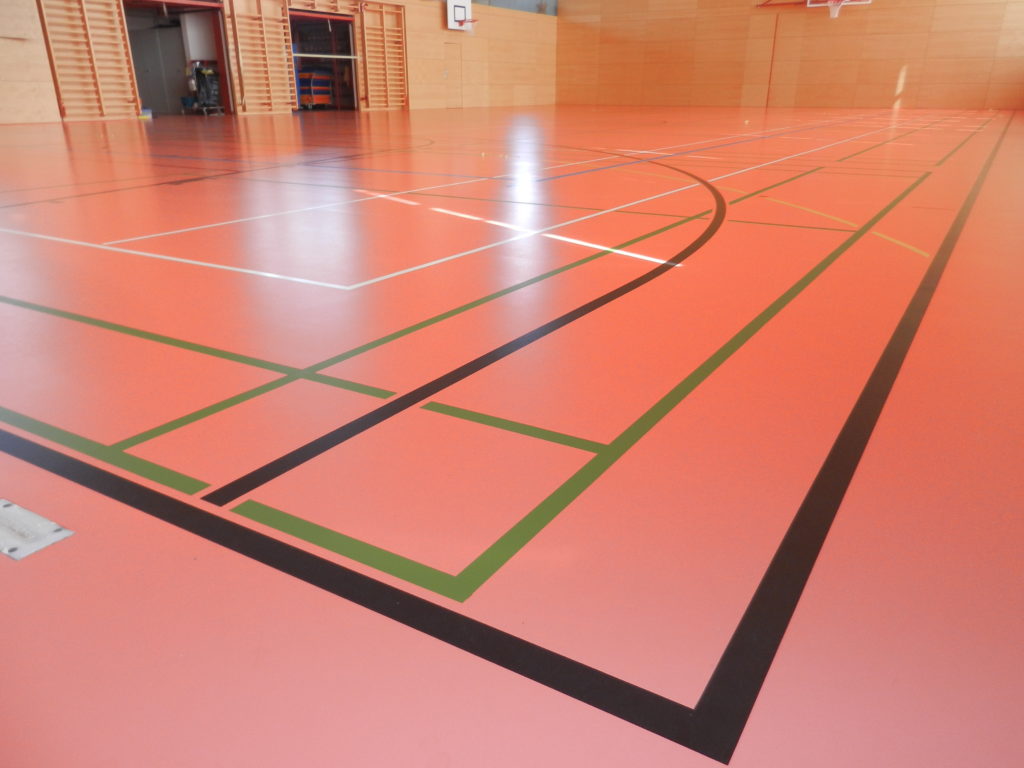Lignes vertes de badminton et ligne noire de basket sur un sol sportif orange