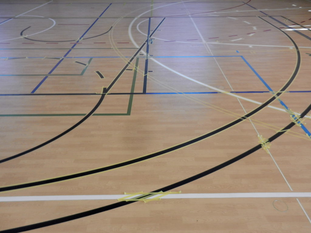 Salle de sport au sol PVC décor bois pendant le marquage, nouveaux arcs de basket peints entre les rubans de masquage