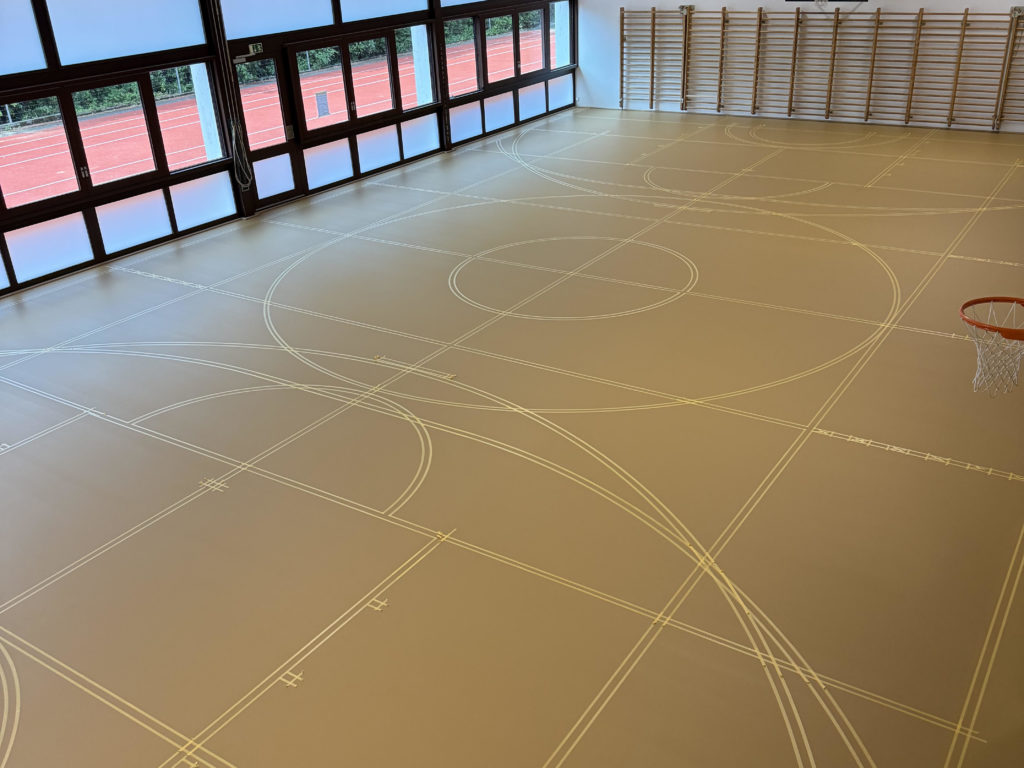 Marquage d'un sol sportif : toutes les lignes de jeu implantées au scotch avant la peinture, vue d'ensemble de la salle