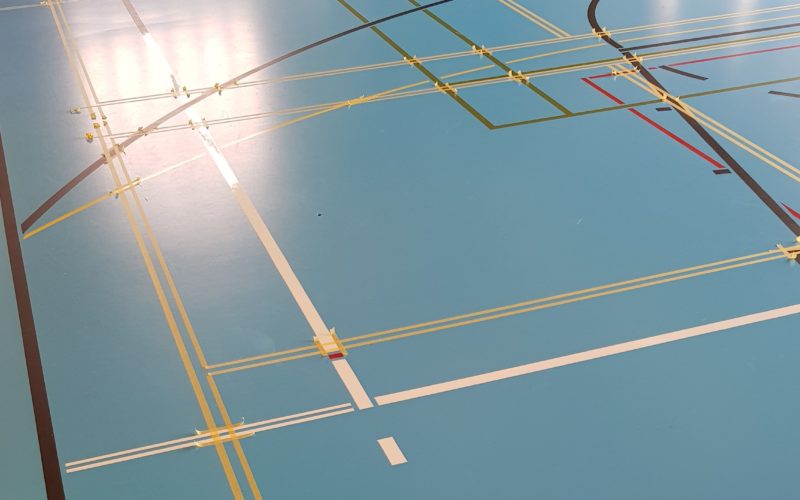Nouveaux terrains de badminton marqués en doubles rubans sur un sol sportif, prêts pour la peinture