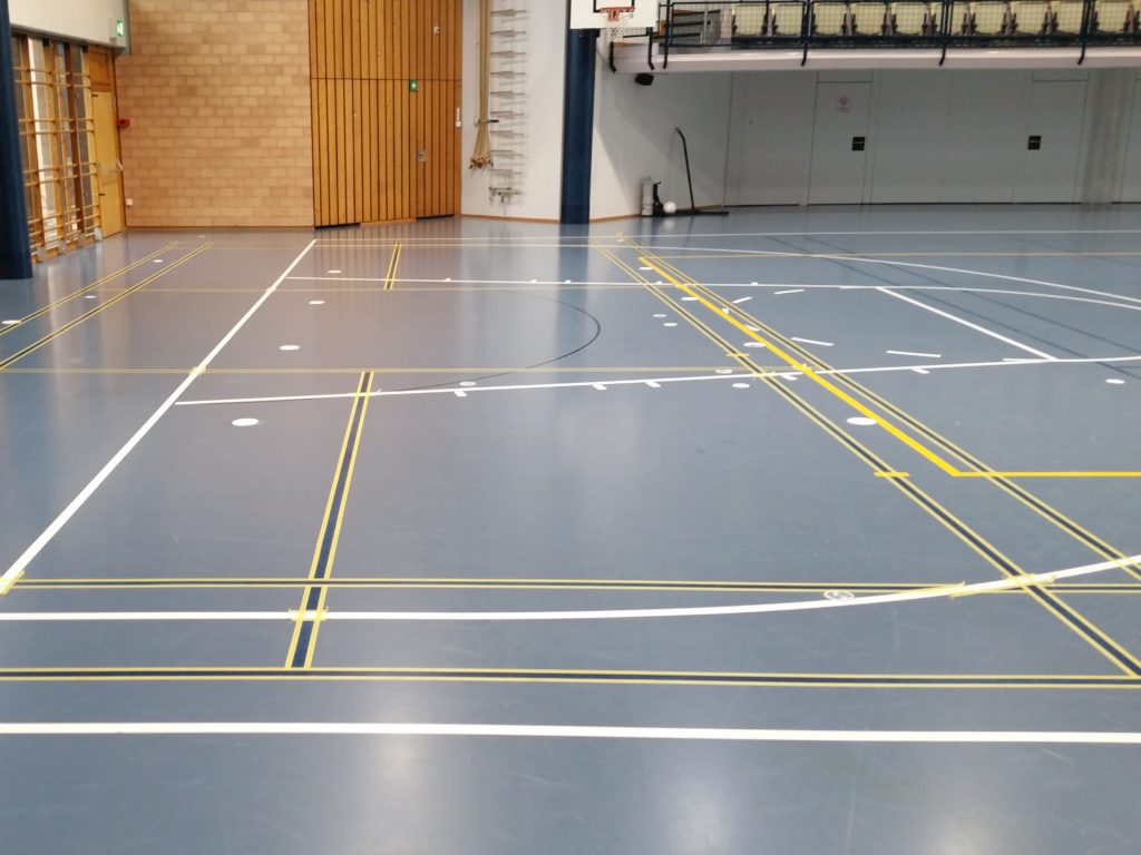 Masquage en doubles rubans des lignes de badminton sur un sol sportif avant la mise en peinture