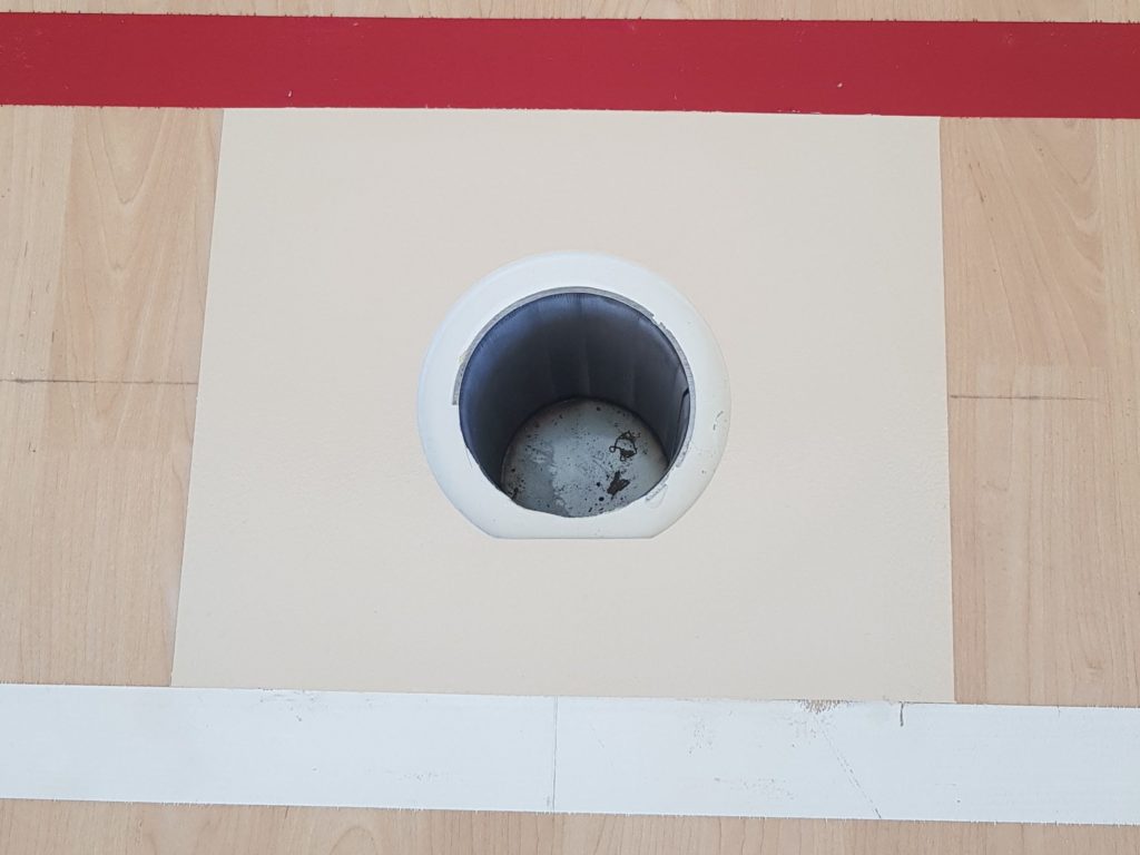 Nouveau pourtour et nouveau couvercle de douille réalisés sur un sol sportif en PVC décor bois, entre deux lignes de jeu