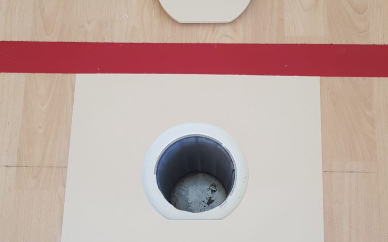 Nouveau pourtour et nouveau couvercle de douille réalisés sur un sol sportif en PVC décor bois, entre deux lignes de jeu