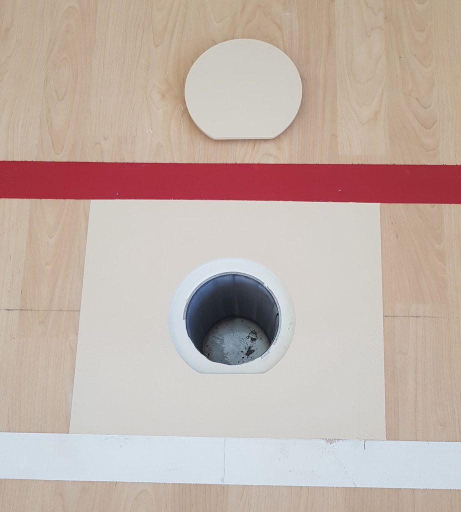 Nouveau pourtour et nouveau couvercle de douille réalisés sur un sol sportif en PVC décor bois, entre deux lignes de jeu