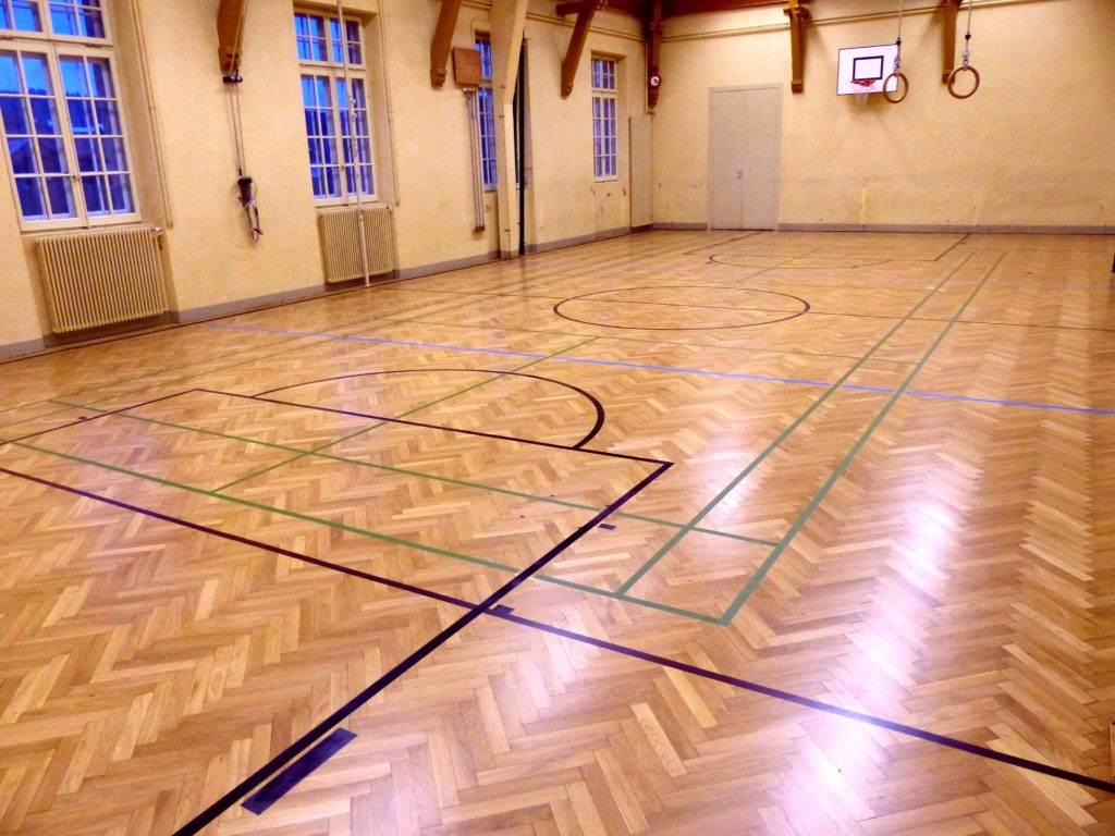 Parquet sportif en chevrons poncé et vitrifié dans une salle de gymnastique ancienne, lignes de jeu refaites