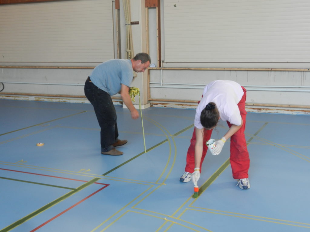 Peinture des lignes de jeu au pinceau entre les bandes de scotch sur un sol sportif