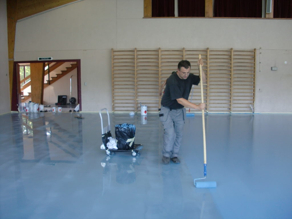 Application au rouleau de la peinture de sol bleue dans une salle polyvalente