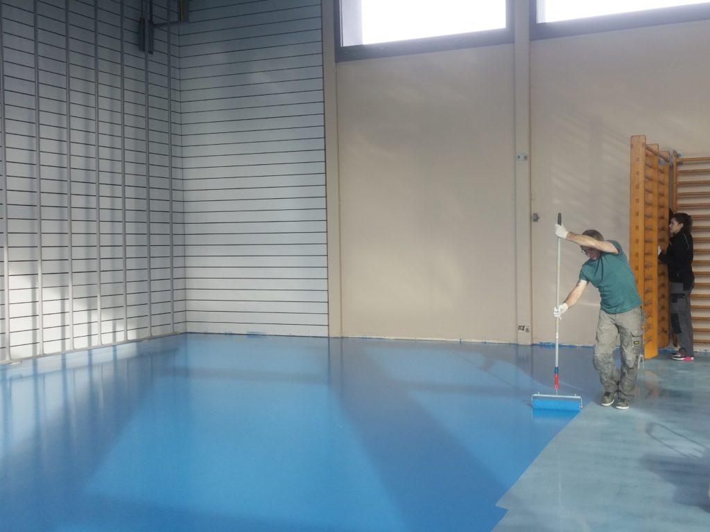 Application au rouleau de la peinture de sol bleu ciel sur un sol sportif en résine