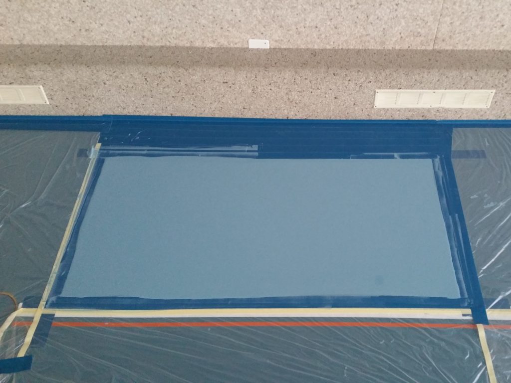 Peinture de sol appliquée sur une zone réparée, cadrée au ruban, reste du sol sportif protégé par des bâches
