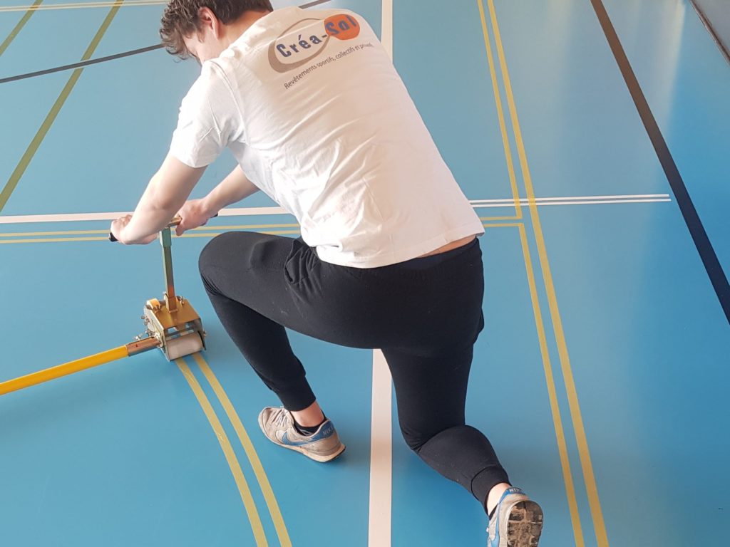 Ouvrier posant le ruban de masquage d'une ligne courbe avec un dérouleur guidé sur un sol sportif