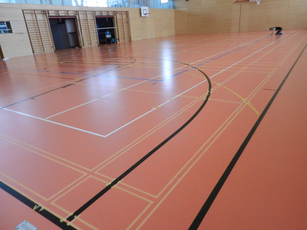 Nouveaux terrains de badminton délimités au scotch sur un sol sportif orange