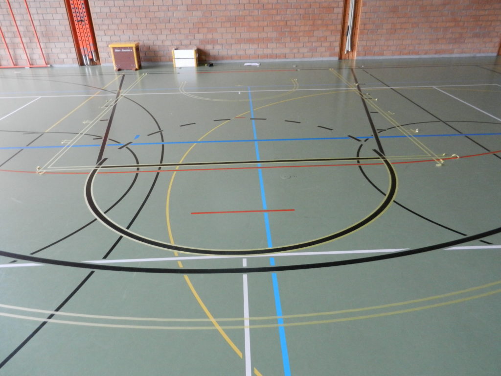 Nouveau tracé de basket délimité au scotch, anciennes lignes encore visibles sur le sol sportif