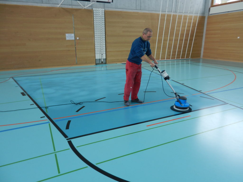 Préparation à la monobrosse d'une raquette de basket sur un sol sportif bicolore, avant le nouveau marquage