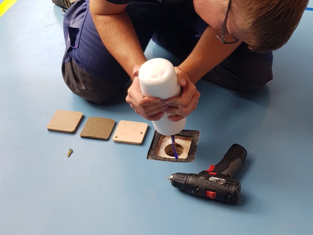Ouvrier injectant du produit dans un percement carré d'un sol sportif, pièces de plancher et de caoutchouc prêtes à reconstituer les couches