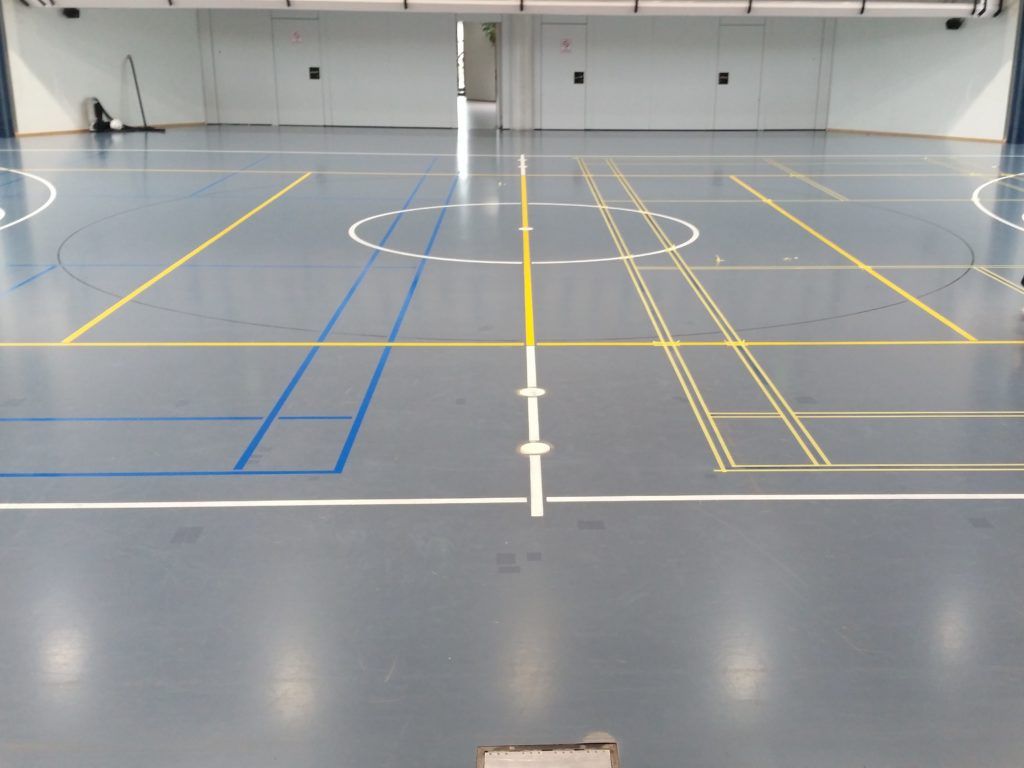 Remarquage de terrains de badminton en bleu ciel, lignes déjà peintes d'un côté et masquage en cours de l'autre