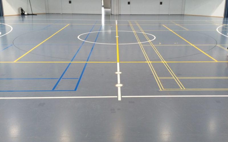 Remarquage de terrains de badminton en bleu ciel, lignes déjà peintes d'un côté et masquage en cours de l'autre