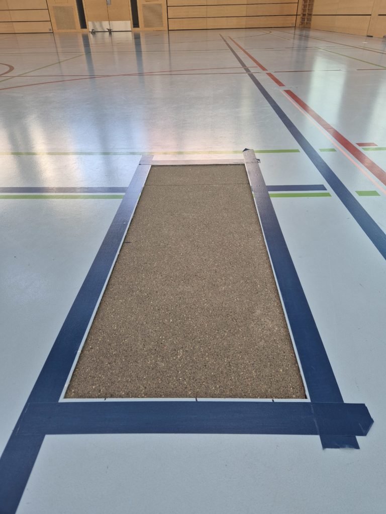 Sous-couche souple en granulés de caoutchouc posée dans la zone réparée d'un sol sportif, pourtour protégé avant le coulage de la résine
