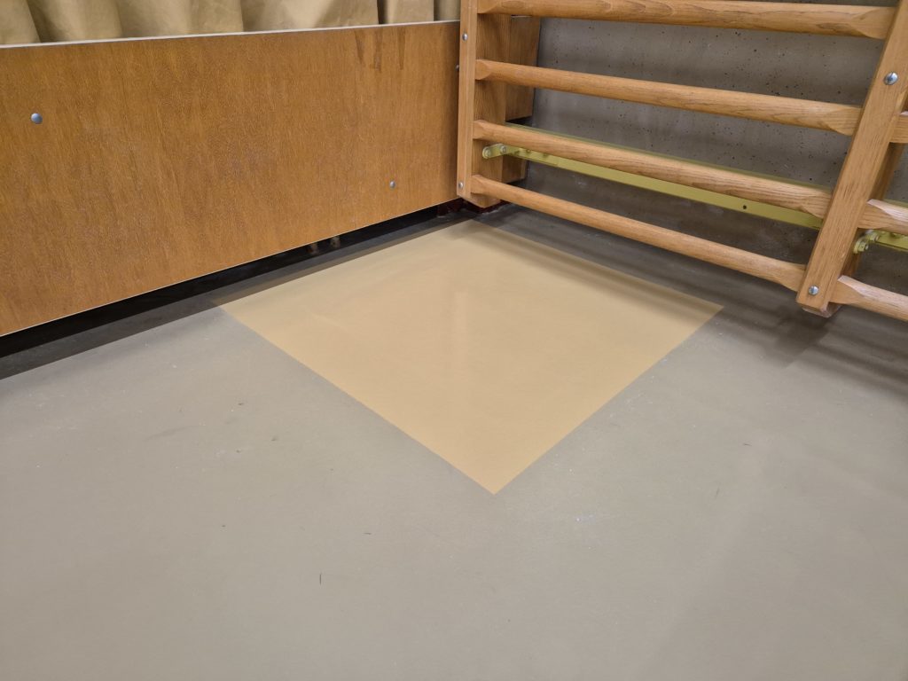 Zone réparée d'un sol de salle de rythmique peinte dans une teinte de base, au pied d'un espalier