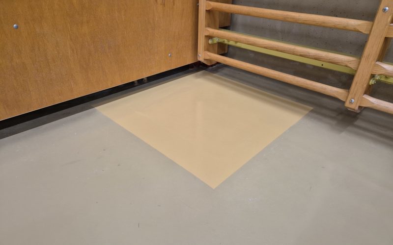 Zone réparée d'un sol de salle de rythmique peinte dans une teinte de base, au pied d'un espalier